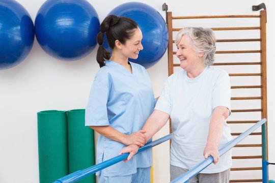 Senior Woman Walking With Parallel Bars With Therapist