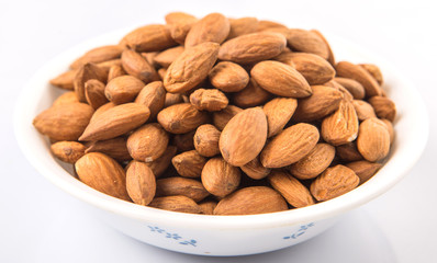 Raw almond nut in a white bowl over white background
