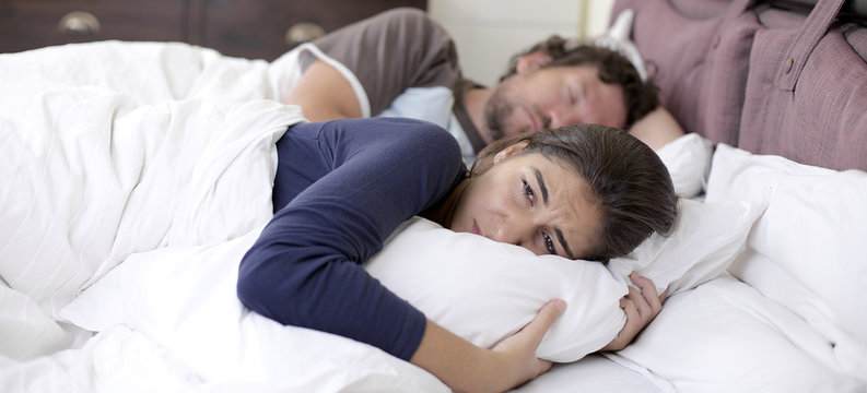 Sad desperate woman in bed while husband is sleeping