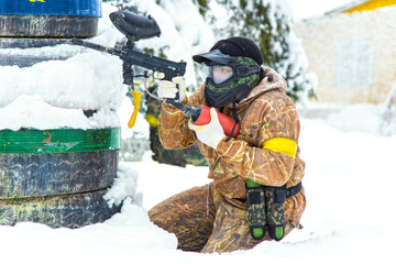 Extreme paintball player aiming behind tyres on snow