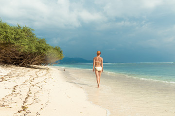 Fototapeta na wymiar Young woman walking along tropical beach