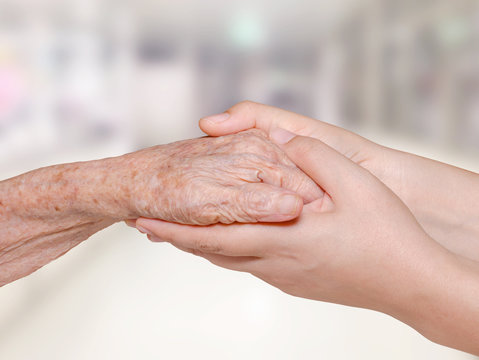 Young nurse holding old patient hand in hospital