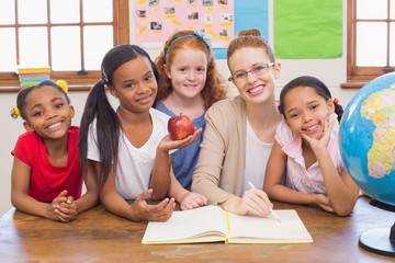 Cute pupils and teacher smiling at camera in classroom