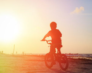 Naklejka premium little boy riding bike at sunset