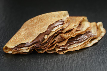 thin crepes or blinis with chocolate cream on slate board - obrazy, fototapety, plakaty