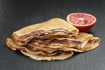 crepes or blinis with chocolate cream and orange on slate board