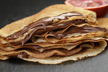 crepes or blinis with chocolate cream and orange on slate board