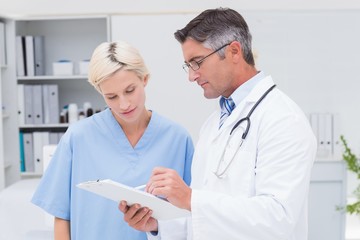 Doctor and nurse discussing over notes on clipboard