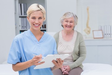 Nurse holding clipboard while female patient sitting in clinic