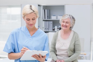Nurse writing on clipboard while patient sitting in clinic