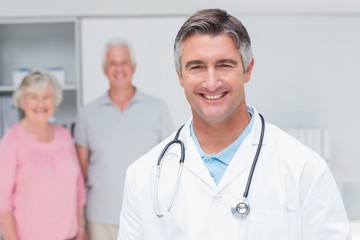 Doctor smiling with senior couple in background at clinic