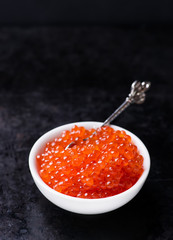 Salmon caviar in white bowl on dark background