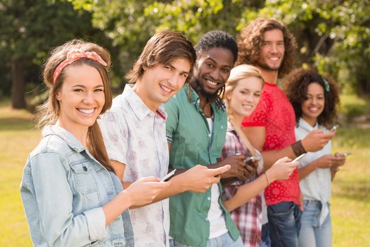 Happy friends in the park using their phones