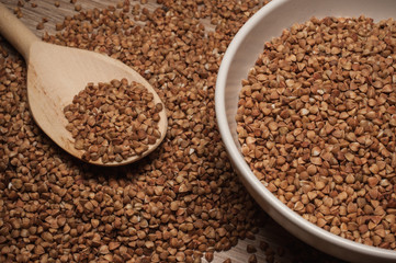 buckwheat groats on wooden spoon next to bowl