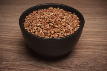 Buckwheat in black bowl on wooden background.