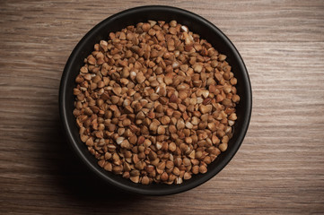Buckwheat in black bowl on wooden background. Closeup.