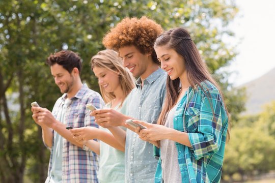 Happy friends in the park using their phones