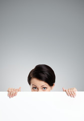 Fototapeta premium Beautiful woman hides behind a huge sheet of white cardboard