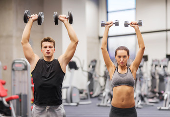 Fototapeta na wymiar smiling man and woman with dumbbells in gym