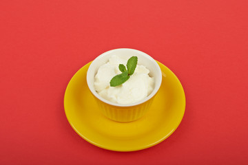 White ice cream in a bowl with mint on a red background
