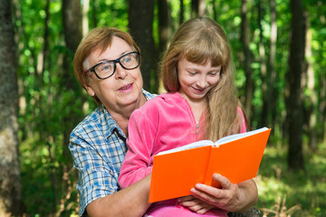 Grandmother and granddaughter reading a book outdoors