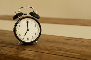 Vintage alarm clock on rustic wood table. Shows 7 o'clock.