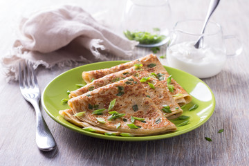 Pancakes with green onions and sour cream on a wooden table