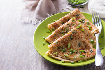 Pancakes with green onions and sour cream on a wooden table