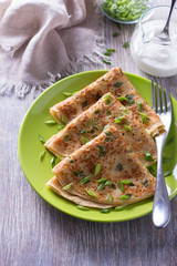 Pancakes with green onions and sour cream on a wooden table
