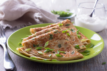 Pancakes with green onions and sour cream on a wooden table