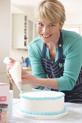 Woman Icing Birthday Cake In Kitchen At Home