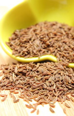 Cumin seeds pouring out of yellow bowl