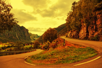 A winding country road with a steep mountain at sunset time.