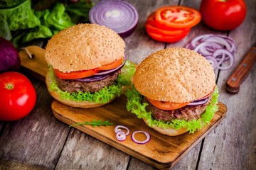 two homemade burgers with fresh vegetables on rustic background