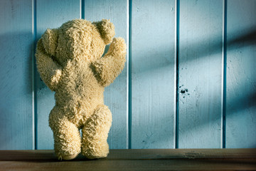 teddy bear stands in front of a blue wall