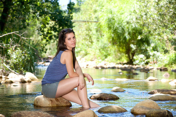 Woman sitting on rock by a stream with bare feet in water