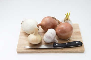 garlic and onions on a wooden board with knife