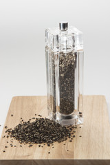 glass mill with black pepper peas on a wooden board, isolated