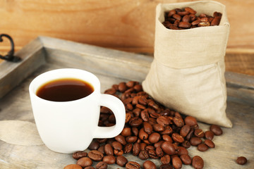 Cup of coffee with beans on tray and rustic wooden background