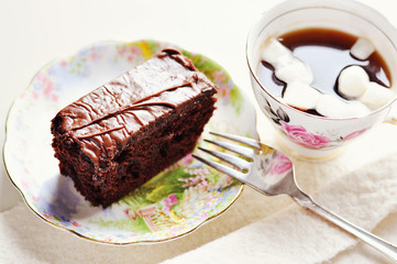 Chocolate cake on a sauser and a cup of coffee with marshmallows