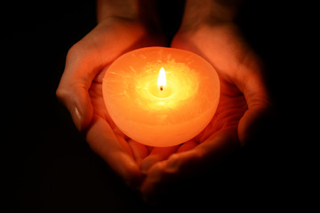 Candle in female hands on black background