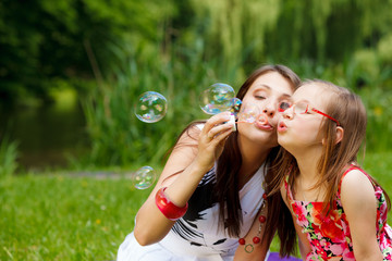 Mother and little girl blowing soap bubbles in park.