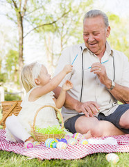 Grandfather and Granddaughter Coloring Easter Eggs on Blanket At