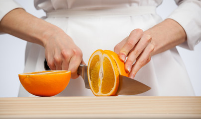 Female hands cutting fresh juicy orange - obrazy, fototapety, plakaty