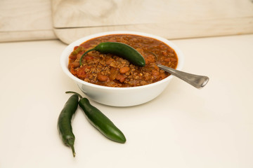 White Bowl of Chili with Two Jalapenos and One on Top