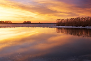 Winter landscape with river, reeds and sunset sky.