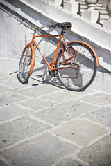 Fototapeta na wymiar Old rusty orange bicycle against a marble wall (Tuscany - Italy)