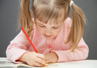 Beautiful little girl drawing with a red  pencil