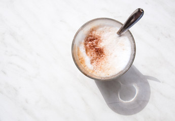 Foamy cappuchino in coffee glass with spoon on white