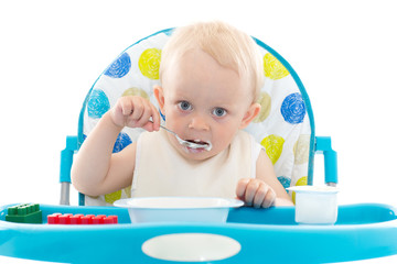 Sweet baby with spoon eats the yogurt.